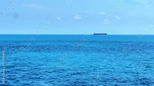 The view of a cargo or tanker ship from afar in the middle of the open blue sea
