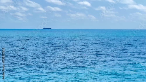 The view of a cargo or tanker ship from afar in the middle of the open blue sea
