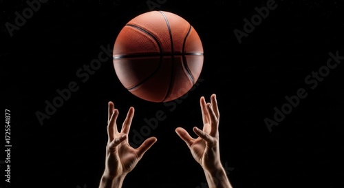Basketball above reaching hands on black, dramatic contrast and directional light, sharp ball texture, shallow depth of field, energetic minimal sports branding