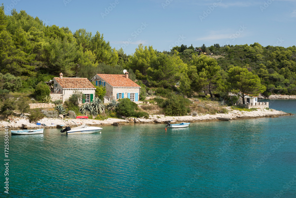 Obraz premium Naturstein-Häuser mit terrakotta-farbenem Ziegeldach, Boote und Kiefernwald an der felsigen Küste mit türkisfarbenem Meer auf der Insel Losinj, Kroatien