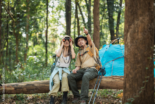 Hiking Asian couple of hikers in outdoor activity wearing backpacks. Woman hiker looking with binoculars smiling happy.