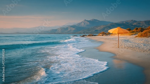 Fototapeta Naklejka Na Ścianę i Meble -  Beautiful sandy beach with orange umbrella and calm sea waves at sunrise near mountains