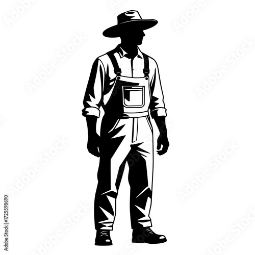 Farmer wearing overalls and a hat stands proudly in a field during the early morning light