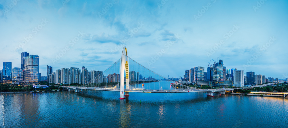 Obraz premium Modern cable-stayed bridge spanning the river with city skyline in at dusk in Guangzhou.