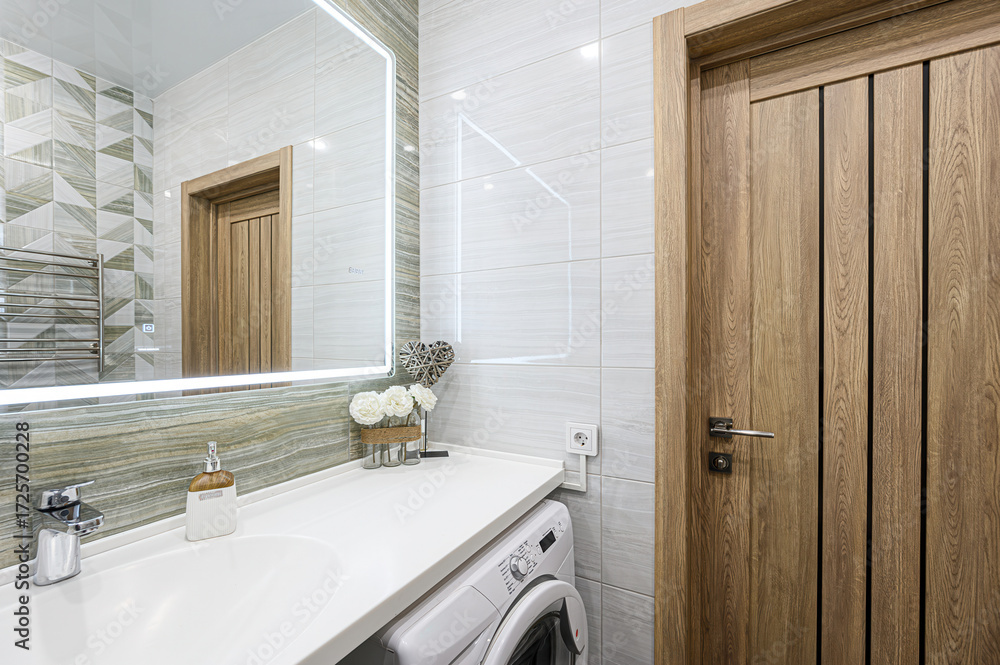 Obraz premium Modern bathroom with a light-up mirror, white countertop, sink, a washing machine, and a wooden door