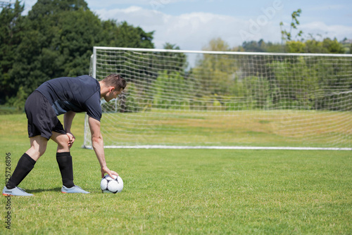Foto Male soccer player in black uniform placing ball on grass pitch beside goal fram