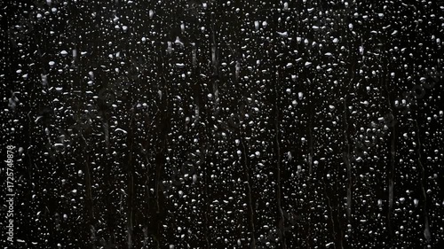 Raindrops cling to a windowpane, creating an abstract pattern of light and shadow