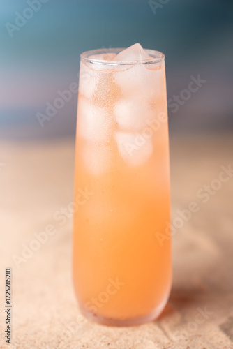 chilled refreshing peach-colored beverage in tall glass with ice cubes on warm soft focus background evoking a summery and inviting atmosphere, bubbly, ocean, sea, backdrop, sandy, blissful, leisure