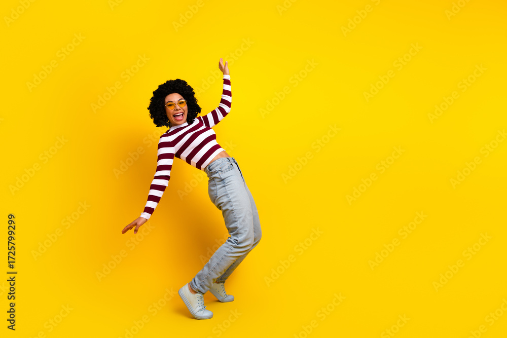 Fototapeta premium Joyful young woman in trendy casual attire posing playfully in front of a vibrant yellow background