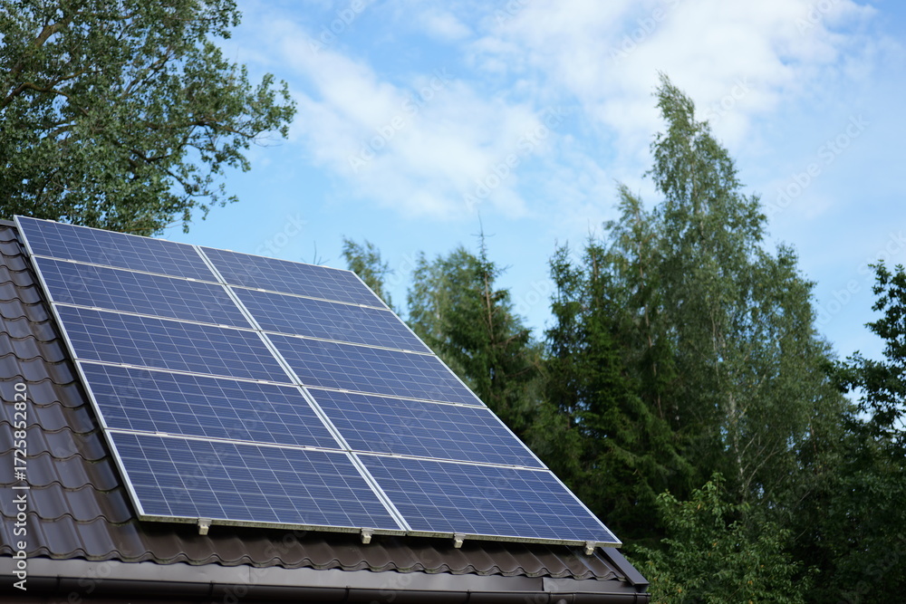 Fototapeta premium Solar panels installed on a roof in a green environment under a bright blue sky during the day