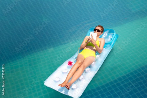 young beautiful woman in bikini enjoy laying in inflamable tube with read on digital tablet and swimming pool in Summer enjoying holidays having sunbath with tan body