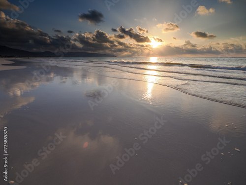 Scenic beach at sunset with clouds reflecting in wet sand and soft waves on the shoreline