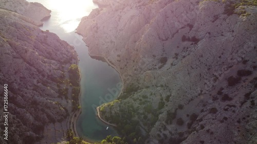 Aerial view of a dramatic canyon with turquoise water surrounded by rugged rocky cliffs and sparse vegetation, taken in Croatia