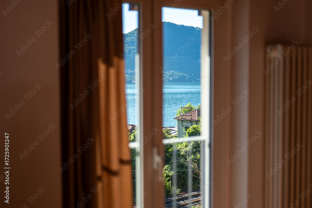 Fototapeta premium Scenic view of a tranquil lake framed by curtains from a cozy room, showcasing mountains and nature during daylight