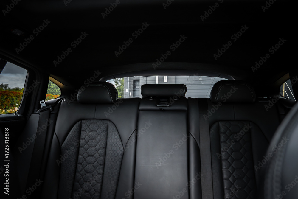 Naklejka premium Close up of BMW X4 rear seats with black leather, hexagonal quilting, visible headrests, and a folded armrest. Modern building seen through rear window.