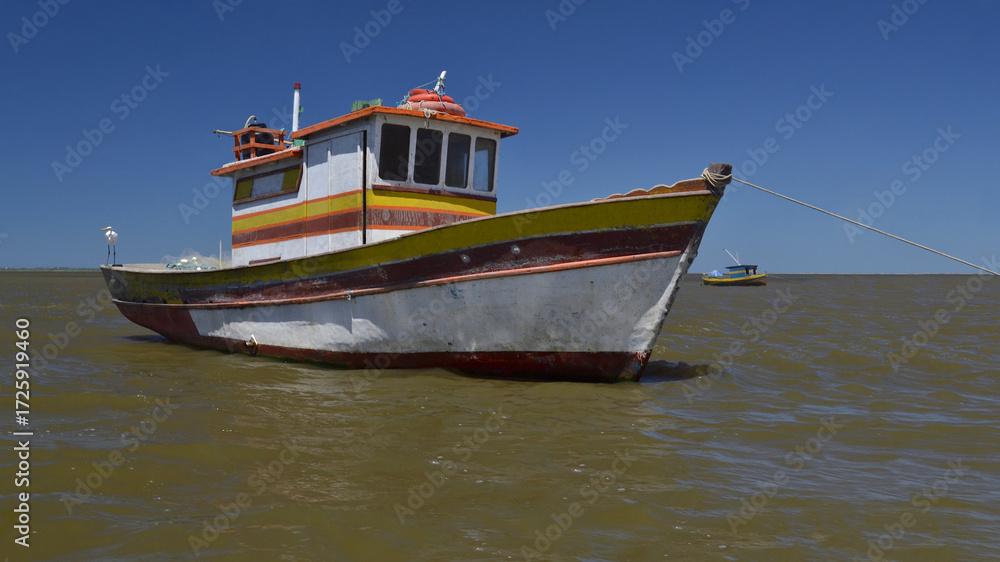 Naklejka premium Old fishing boat in the middle of the river with beautiful sunny blue sky and sea in the background.