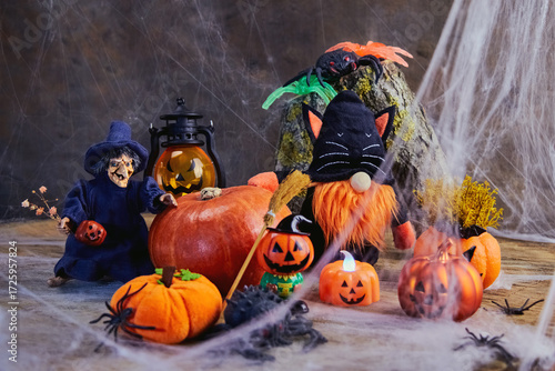 halloween, a cheerful witch with flowers and a gnome in a black cat costume stand near a big pumpkin at a noisy cobweb party with pumpkins and spiders, All Saints Day, horizontal, creative focus