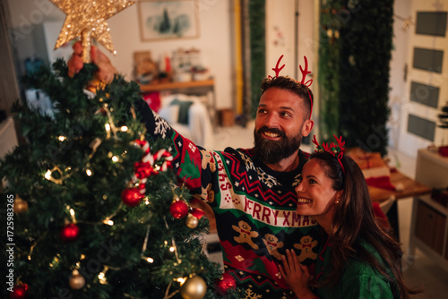 Happy couple placing star on top of decorated christmas tree