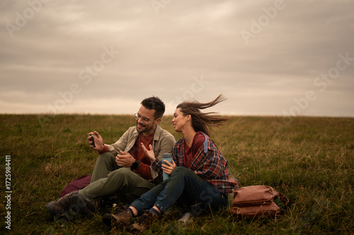 Hikers resting on meadow and using smartphone