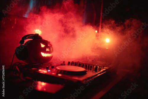 A carved Halloween pumpkin with glowing eyes and headphones sits on a DJ turntable, illuminated by red smoke and lights.