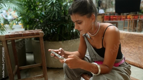 A young woman is comfortably engaged with her smartphone while relaxing in a pleasant environment,