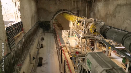 Underground metro tunnel interior during construction with concrete segment lining, utility cables, ventilation ducts, and dim industrial lighting in progress of large infrastructure engineering proje