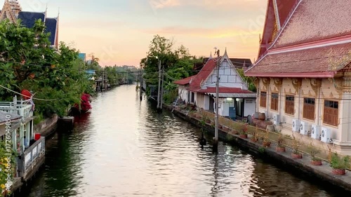 A canal winds through a village in thailand at sunset