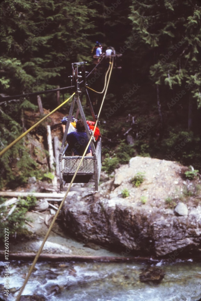 Naklejka premium People riding vintage cable car over a rushing river, crossing forest in remote wilderness, adventure travel