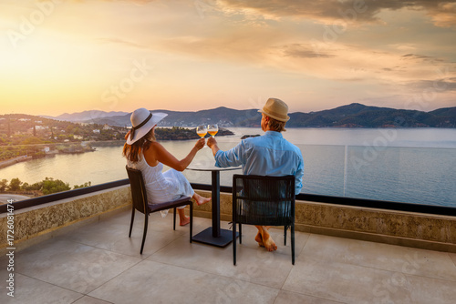 A elegant holiday couple enjoys the beautiful summer sunset in the mediterranean sea with a glass of wine, romantic honeymoon vacation concept