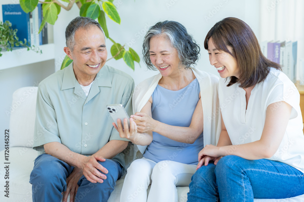 Obraz premium リビングでスマホを見るシニア夫婦と子供