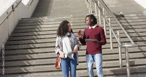Stepping onto staircase, diverse friends descending steps while comparing tablet and smartphone