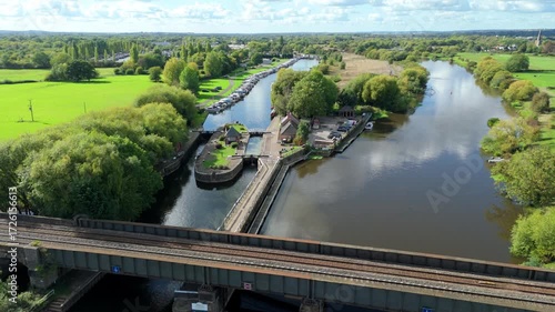 Aerial view of canal lock gate system on River Trent, narrow boat vacation and infrastructure, rolling green rural landscape sunny evening near Nottingham, United Kingdom