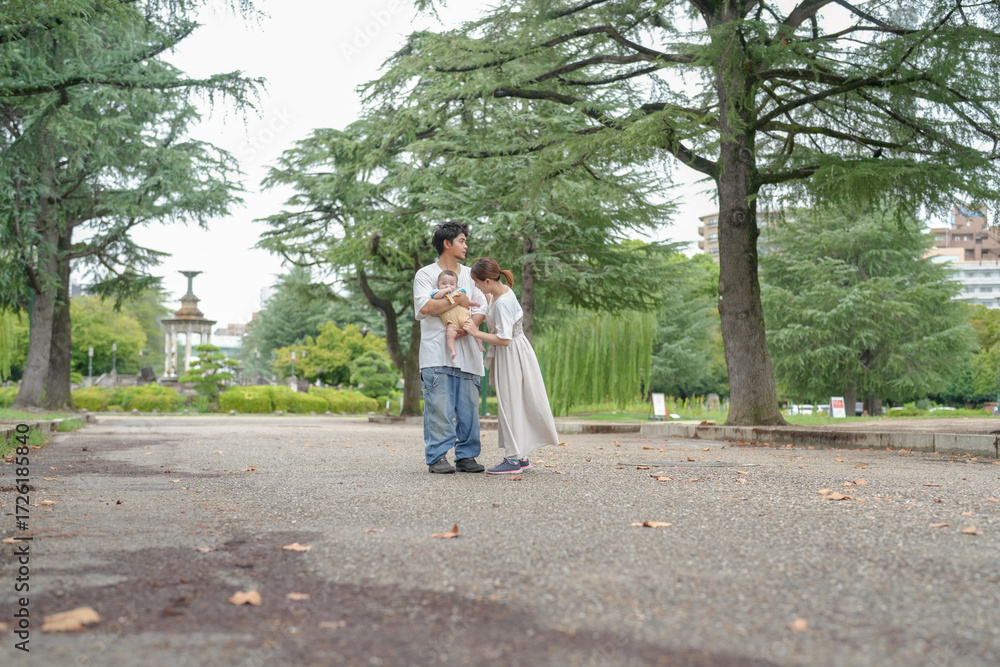 Fototapeta premium A couple holding a baby in a park. The baby is wearing a white shirt. The couple is walking on a path in the park