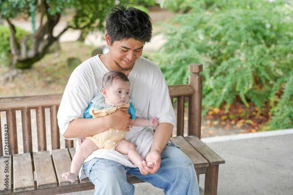 Fototapeta premium A man is holding a baby on a bench. The baby is wearing a blue shirt