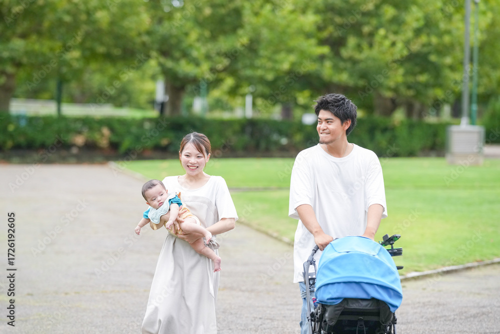 Obraz premium A young couple is walking with a baby in a stroller. The baby is wearing a blue shirt