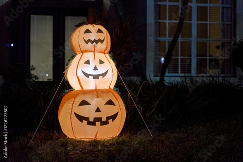 Three smiling jack-o-lantern inflatables are tied and glowing outside a house after dark. Warm light and orange color create a cheerful, festive Halloween yard display.