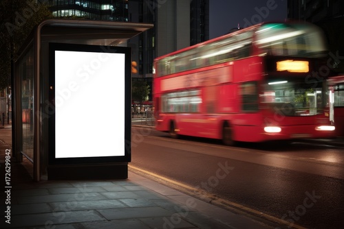 A blank billboard at a city bus stop at night with a red double-decker bus passing by on the street