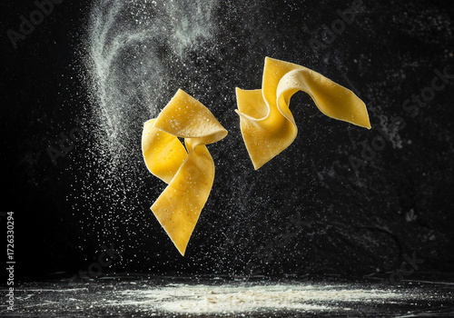 Fresh pasta sheets falling are surrounded by flour against dark backdrop showcasing culinary arts