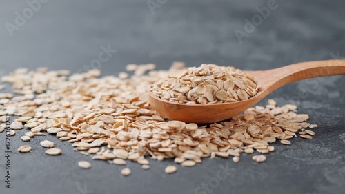 oat flakes in a wooden spoon on a black marble background.  dry rolled oats or rolled oat in a wooden spoon on a dark kitchen table.
