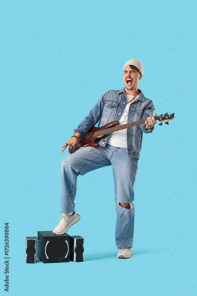 Naklejka premium Young man with speakers playing electric guitar on blue background