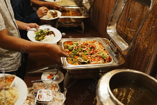 People are serving themselves from a buffet with vegetables and rice.
