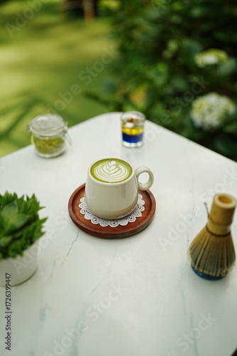 A cup of matcha latte with latte art on a wooden plate.