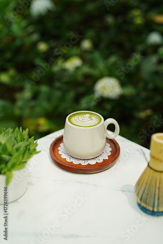 A cup of matcha latte with latte art on a wooden plate.
