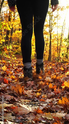 Mesmerizing cinematic low-angle tracking video along winding autumn path. Gender-neutral feet in hiking boots step on crimson maple leaves. Golden hour light, concept of serene wellness journey