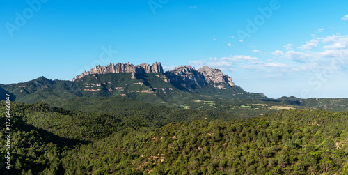 Wallpaper Mural A stunning view of the Montserrat mountain range in Catalonia, Spain, under a clear blue sky. The jagged peaks rise dramatically above the lush green fields. Torontodigital.ca
