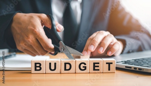 Hands adjust wooden “BUDGET” blocks over dollar bills—scissors poised to cut between “D” and “G” evoke financial reduction, expense control, and strategic adjustment in minimalist economic symbolism c