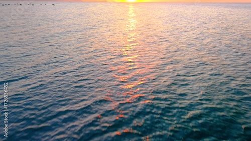 Tilt-up shot from ocean with gentle ripples to golden sunrise sky, clear weather, tranquil seascape glowing in natural light. Royalty high-quality free best stock of the sun rising up