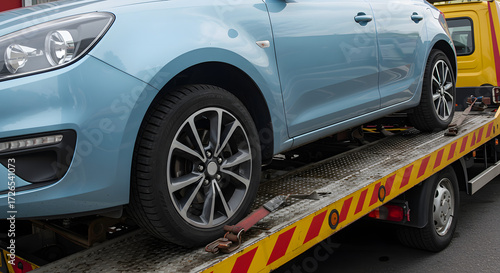 Close up of a light blue car being loaded onto a tow truck flatbed