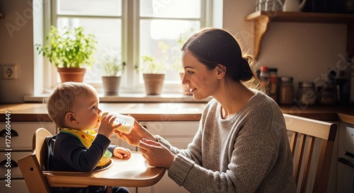 A young woman feeding a baby in a high chair in a cozy kitchen with plants and wooden furniture.