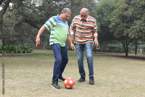 Indian senior old friends playing football in garden 